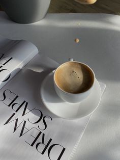 a cup of coffee sitting on top of a white saucer next to a book