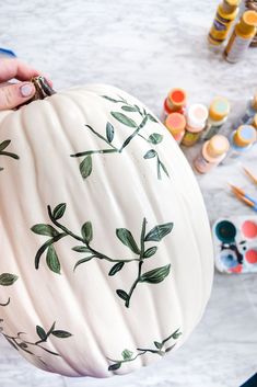 a painted pumpkin being held by someone's hand with other paint and supplies on the table