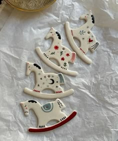 three ceramic rocking horse ornaments sitting on top of a table next to a gold plate