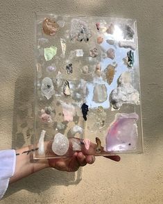 a person holding a paintbrush in front of a clear box filled with different colored rocks