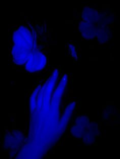 a person's hand with dark blue nail polish and flowers in the background at night