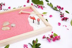 a pink sand tray with two flamingos in it and some flowers on the side