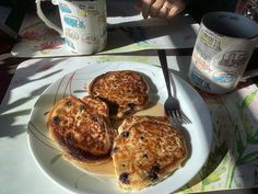 three pancakes on a plate with butter and blueberries next to a cup of coffee