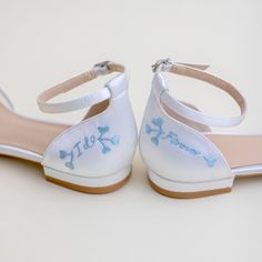 a pair of white shoes with blue flowers on the bottom and one has a bow at the ankle