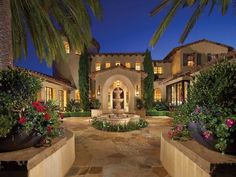 a large house with lots of plants and trees in front of it at night time