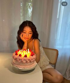 a woman sitting in front of a cake with lit candles