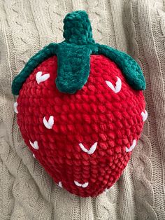 a red knitted strawberry sitting on top of a white blanket