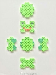 four pieces of green perler beads sitting on top of a white table next to each other