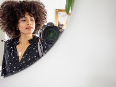 a woman holding a camera in front of a mirror with a plant on the wall behind her