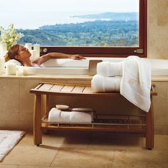 a woman laying in a bathtub next to a window with a mountain view behind it