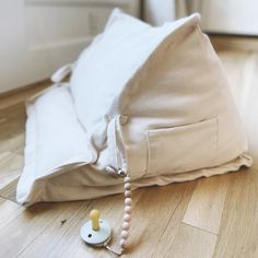 a white pillow laying on top of a wooden floor next to a beaded necklace