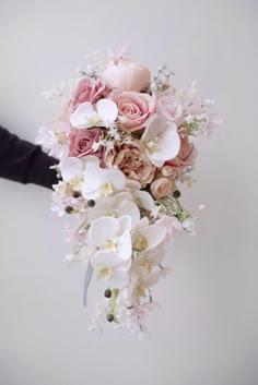 a bridal bouquet with pink roses and white orchids is being held by someone's hand