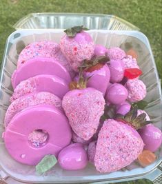 a plastic container filled with pink donuts covered in sprinkles and strawberries