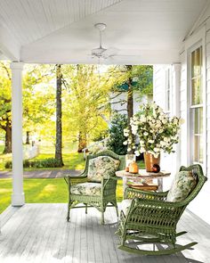 a porch with wicker rocking chairs and flowers on the table in front of it