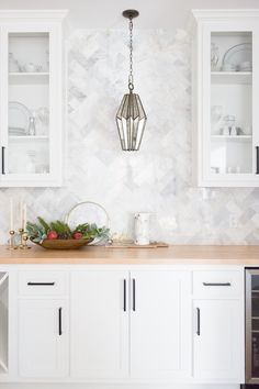 a kitchen with white cabinets and marble backsplash, hanging light fixture over the counter