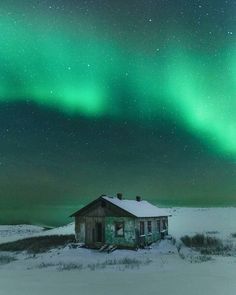 an old cabin in the middle of nowhere with green and red aurora lights above it