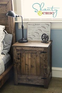 a nightstand with a lamp on top of it next to a bed