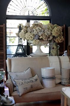 a living room filled with lots of furniture and flowers on top of pillows in front of a window