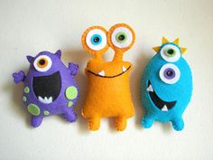 three stuffed monsters are lined up next to each other on a white surface, one is orange and the other is blue