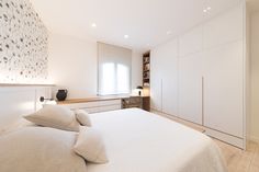 a white bed sitting in a bedroom next to a wooden shelf filled with drawers and pillows