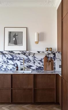 a kitchen with marble counter tops and wooden cabinets in the corner, along with an art work on the wall