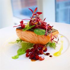 a white plate topped with a piece of salmon covered in greens and red berries on top of it