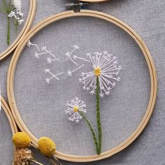 three embroidery hoops with dandelions in them on a gray tablecloth next to flowers