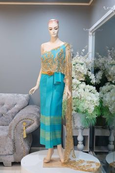 a mannequin wearing a blue and gold dress in front of a couch with flowers