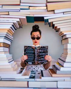 a woman is holding up a book in front of her face while surrounded by stacks of books