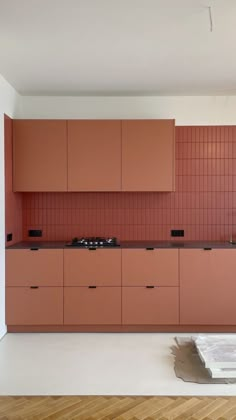 an empty kitchen with wooden floors and pink cabinets on the wall, next to a stove top oven