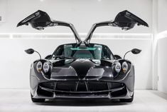 the front end of a black sports car in a white room with two doors open