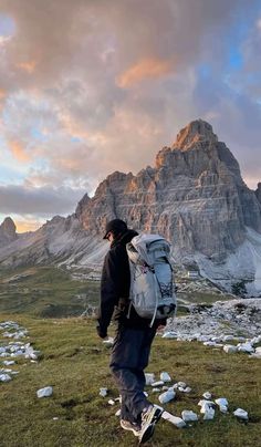 a man with a backpack is walking on the grass in front of a mountain range