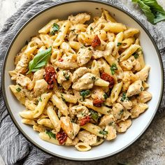 a bowl full of pasta with chicken and tomato sauce on the side next to a towel