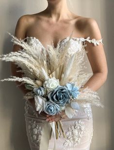 a woman in a white dress holding a bouquet with feathers and flowers on her chest