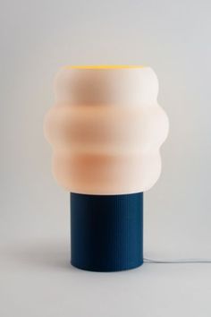 a blue and white lamp with a yellow light on it's side next to a gray wall