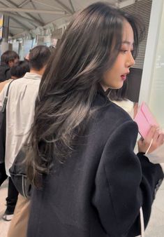 a woman with long dark hair standing in front of a wall holding a cell phone