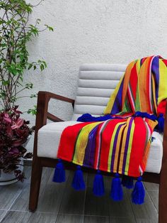 a colorful blanket sitting on top of a wooden chair next to a potted plant