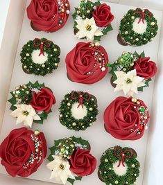 twelve decorated cupcakes in a white box with red roses and green wreaths