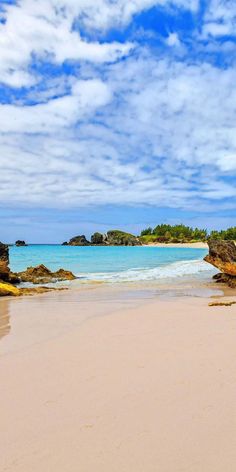 a sandy beach with blue water and white clouds