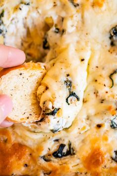 a hand holding a piece of bread with cheese and spinach on it in a casserole dish