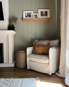 a white chair sitting next to a fireplace in a living room with pictures on the wall