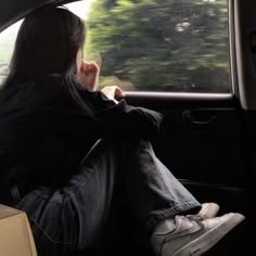 a woman sitting in the passenger seat of a car looking out the window at trees