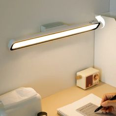 a person writing on a piece of paper in front of a desk lamp that is turned on