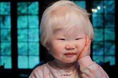 a young child with blonde hair is holding his hand up to his face and looking at the camera