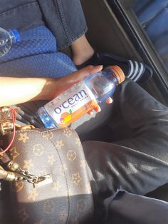 a person sitting in the back seat of a car holding a water bottle and purse