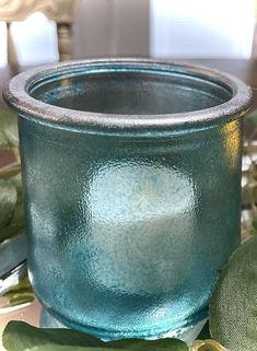 a blue glass bowl sitting on top of a table next to green leaves and flowers