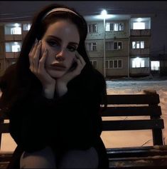 a woman sitting on top of a wooden bench in front of a building at night