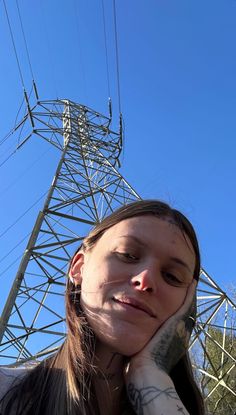 a woman with tattoos on her arm standing in front of an electric tower and looking at the camera