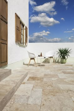 an outdoor patio with chairs, table and potted plant on the side of it