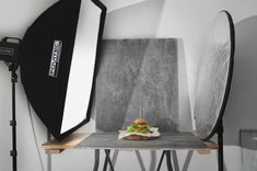 a hamburger sitting on top of a wooden table next to a camera and lighting equipment